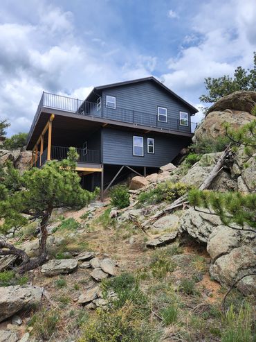 Modern dark gray house built on a rocky hillside with elevated deck